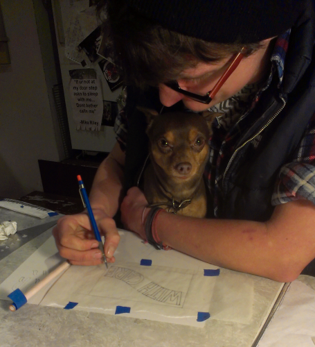 a person seated at a table trying to draw with a small dog on their lap